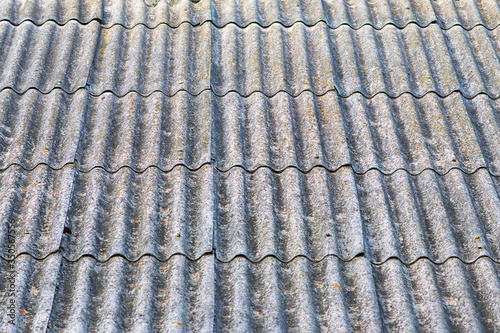Close-up view of old wavy slate roof with moss. Texture of old slate with moss. Shed roof covered with old asbestos sheets. Outdoor interior. Texture of old roof, slate background