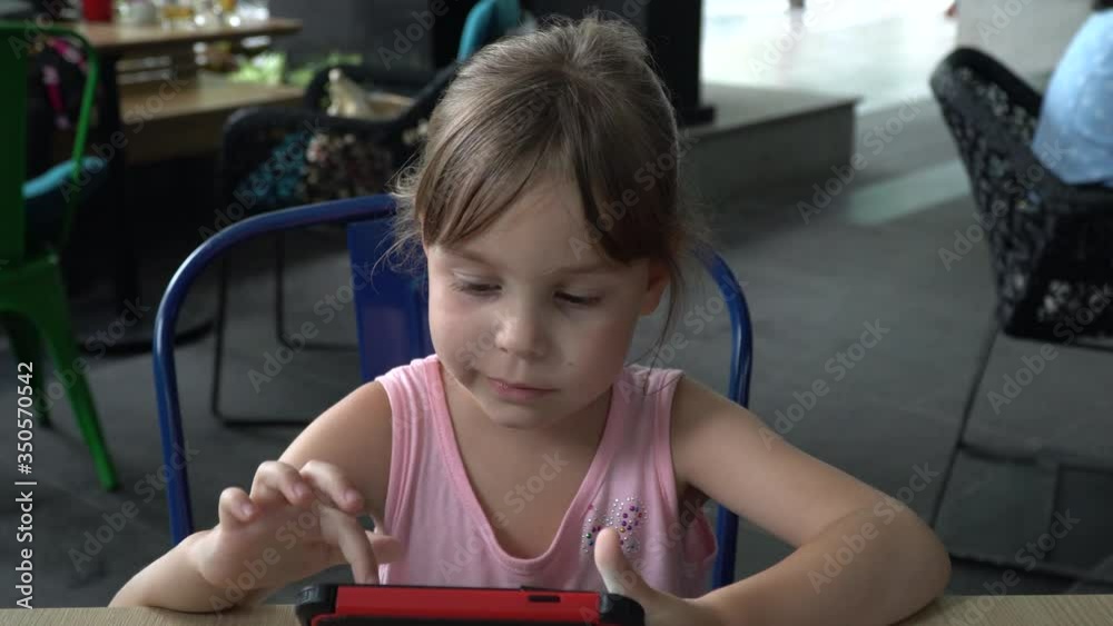Portrait of a child 5-6 years. A girl with blond hair, Russian, sits at the table and holds a cell phone.