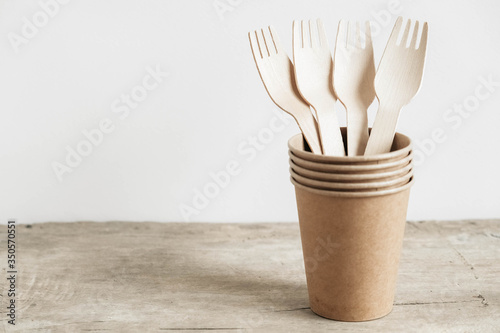 Wooden forks and paper cups on wooden background. Eco friendly disposable tableware. Also used in fast food, restaurants, takeaways, picnics. Copy, empty space for text