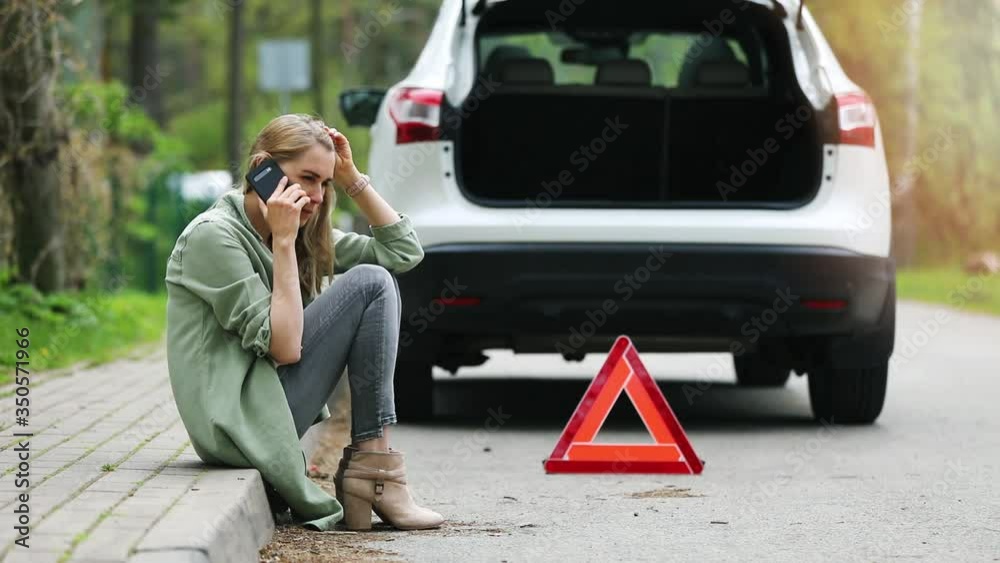 woman is sitting on the side of the road and calling for help because broken car