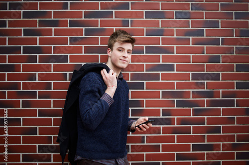 Young man standing at brick wall with smartphone in hand
