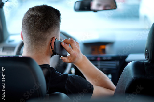 a guy, a young man in a black t-shirt with a black mask sitting behind the wheel, talking on the phone, during the day, rear view © Veronika