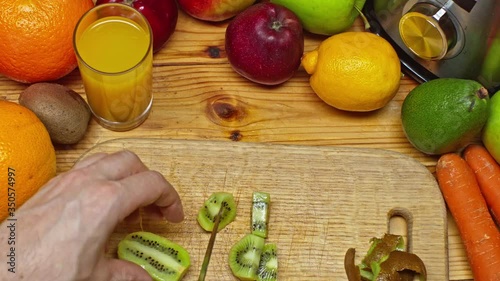 Top view of male hands cutting a kiwi with a knife on a cutting board with a variety of fresh food on the table. Slow Motion Footage.