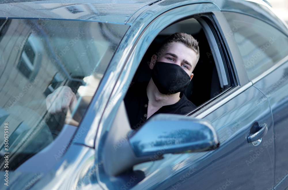 young man, handsome guy sitting in a car driving in a black t-shirt in a black mask looking out the open window, road trip