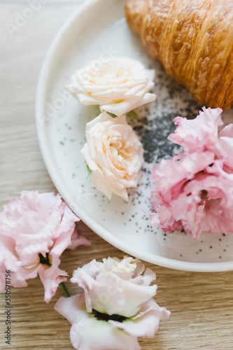 Croissant on a white plate with flowers. Nice breakfast. Concept of coffee shop and flower shop.