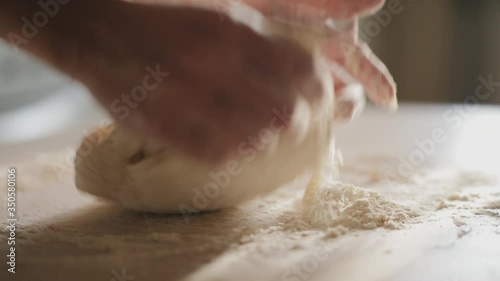 Closeup of female hands kneading dough in flour on the table, slow-motion