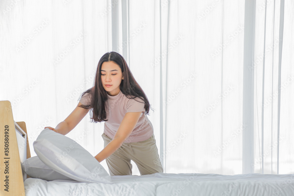 Asian lady making bed in her morning routine after wake up for tidying up the bedroom in soft light with copy space Asian lady making bed in her morning routine after wake up for tidying up the bedroom in soft light with copy space