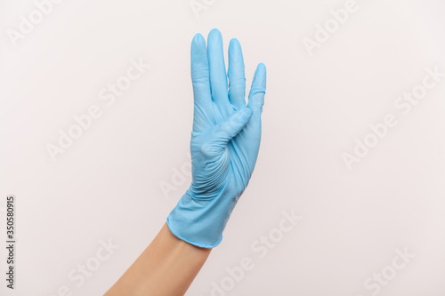 Profile side view closeup of human hand in blue surgical gloves showing number four 4 with hand. indoor, studio shot, isolated on gray background.