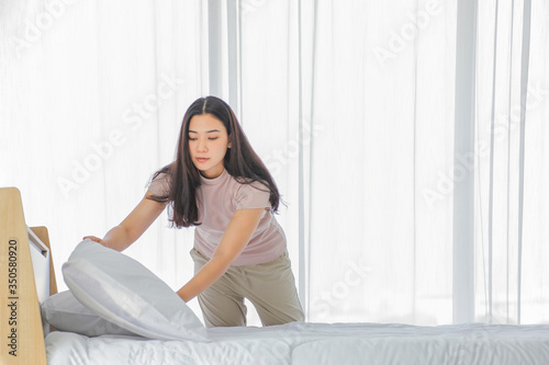 Asian lady making bed in her morning routine after wake up for tidying up the bedroom in soft light with copy space