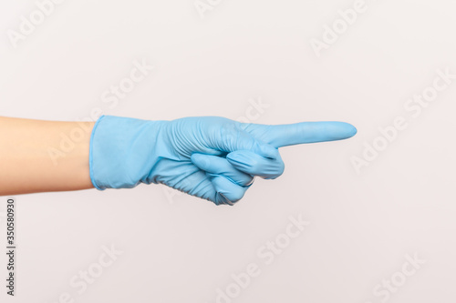 Profile side view closeup of human hand in blue surgical gloves showing or pointing ot someting with finger. indoor, studio shot, isolated on gray background.