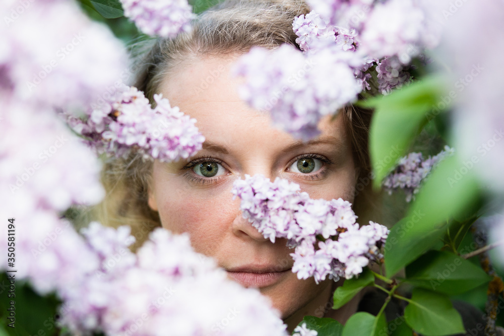 Young blonde woman face behind lilac bush in blossom Young blonde woman face behind lilac bush in blossom