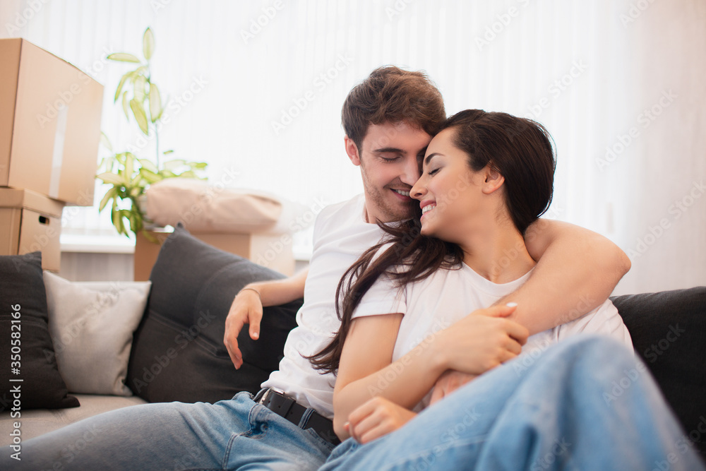 a happy young married couple moves to new apartment. They are sitting on the sofa and looking at their new home.