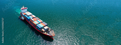 Aerial ultra wide photo of Container cargo Ship carrying load in truck-size colourful containers in deep blue open ocean sea  © aerial-drone