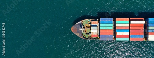 Aerial ultra wide photo of Container cargo Ship carrying load in truck-size colourful containers in deep blue open ocean sea 