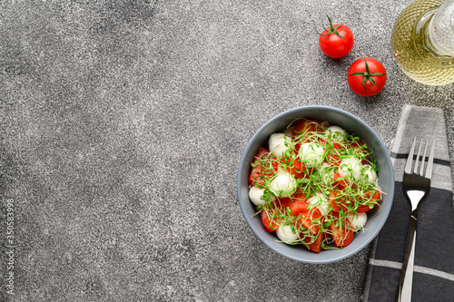 Italian food. Delicious caprese salad with mozzarella cheese, cherry tomatoes and arugula microgreens. Top view with copy space. Gray stone background.