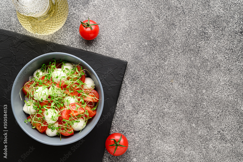 Italian food. Delicious caprese salad with mozzarella cheese, cherry tomatoes and arugula microgreens. Top view with copy space. Gray stone background.