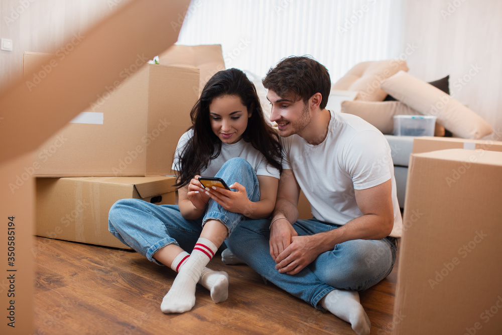 Young couple moving to a new house using smartphone around cardboard boxes Young couple moving to a new house using smartphone around cardboard boxes