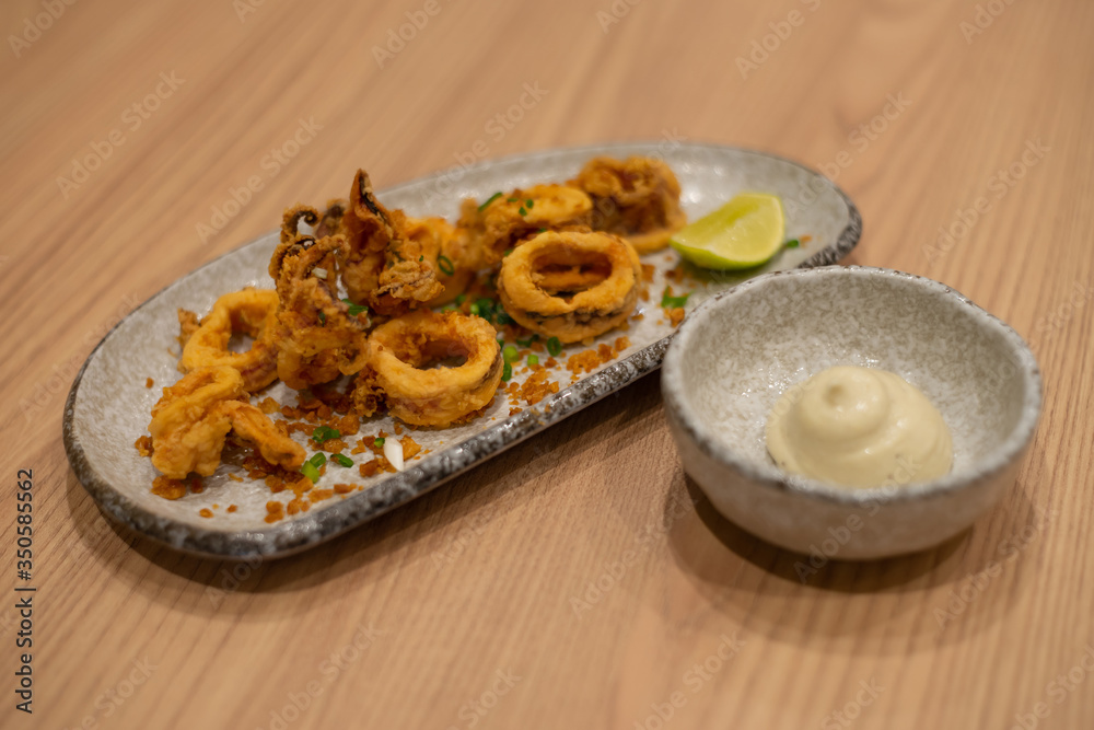 Fried squid rings with lemon on wooden table as appetizer seafood background.