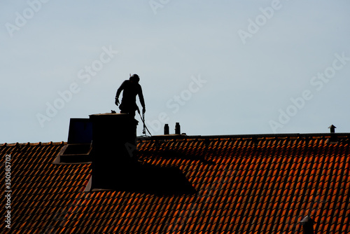 Silhouette of a chimney sweeper on top of a roof..