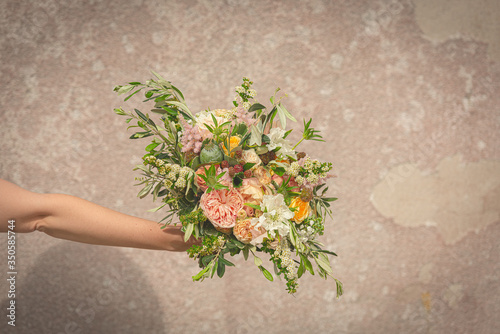Fotografi Hand holding a beautiful wedding bouquet in front of a rustic wall