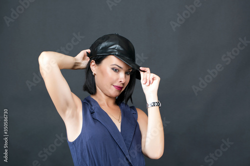 Beautiful young woman in a pretty blue dress and a black leather hat on a grey background