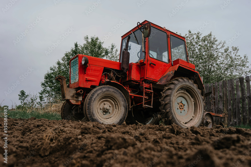 A red tractor stands on a plowed field of dark brown color | KOROVYAKOVA, SVERDLOVSKAYA OBLAST - 9 MAY 2020. A red tractor stands on a plowed field of dark brown color | KOROVYAKOVA, SVERDLOVSKAYA OBLAST - 9 MAY 2020.