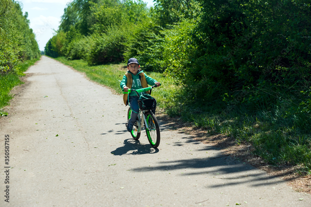 Naklejka premium Boy on bicycle at summer asphalt road. Kid cycling outdoors. Summer sport activity concept. Soft focus