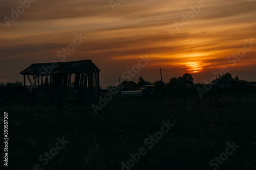 Silhouette of a wooden building in the late evening during the red sunset in the village | KOROVYAKOVA, SVERDLOVSKAYA OBLAST - 9 MAY 2020.
