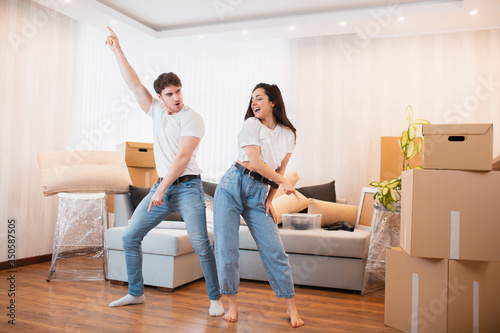 H appy husband and wife have fun swirl sway relocating to own apartment together, relocation concept. Overjoyed young couple dance in living room near cardboard boxes entertain on moving day, photo