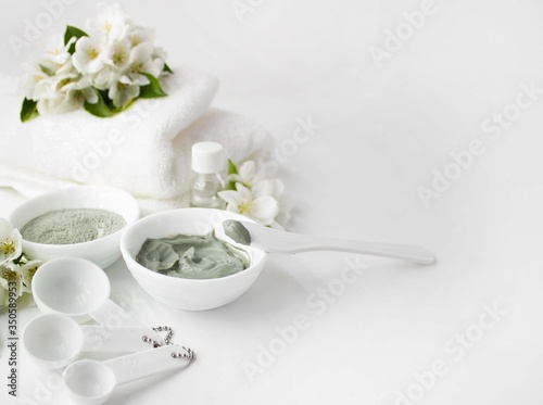 Home spa. Natural clay facial mask, aromatic oil and a fresh white towel on a white background. Empty space for text