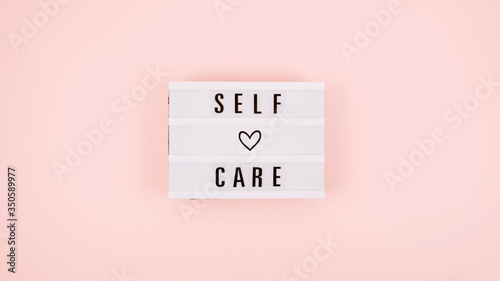 Self-care word on lightbox and flower narcissus on pink background flat lay. Take care of yourself.