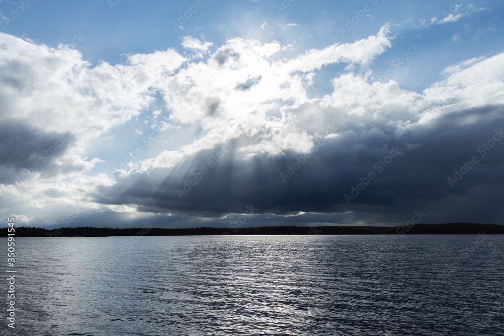 View of thunderstorm clouds above the lake. Cloudy sunset with sunbeams and blue sky.