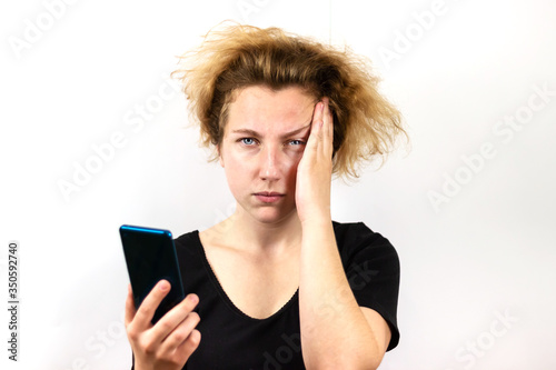 A girl with yellow hair is talking on a video link on a smartphone and with a serious thoughtful expression on her face, putting her hand to her temple, head, on a white background. photo