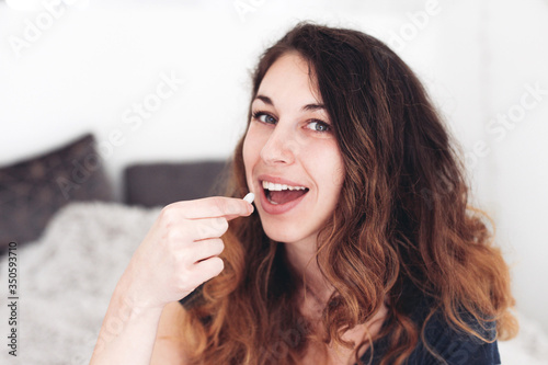 Portrait of a young woman talking a pill. A woman looks happy and content, sitting on a bed in a room