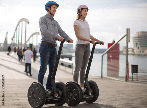 young couple guy and girl are walking on the segway along the board paved promenade in the port of a European city photo
