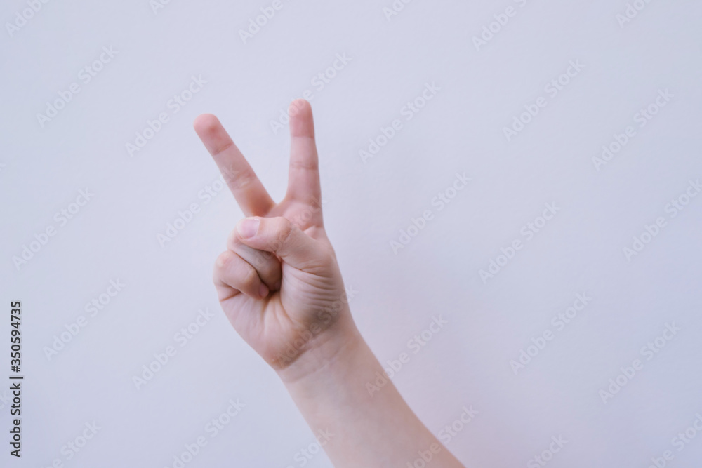 A child's hand shows a victory gesture on a white background. Two fingers up. A child's hand shows a victory gesture on a white background. Two fingers up.