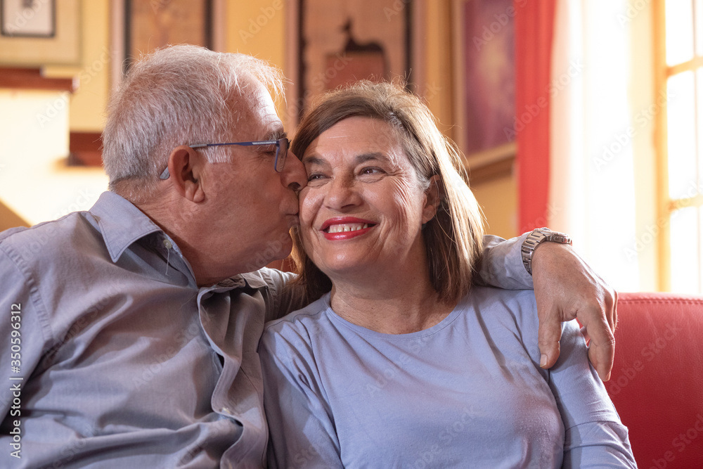 coppia di anziani si abbraccia felice e sorride nel divano del salotto di casa coppia di anziani si abbraccia felice e sorride nel divano del salotto di casa