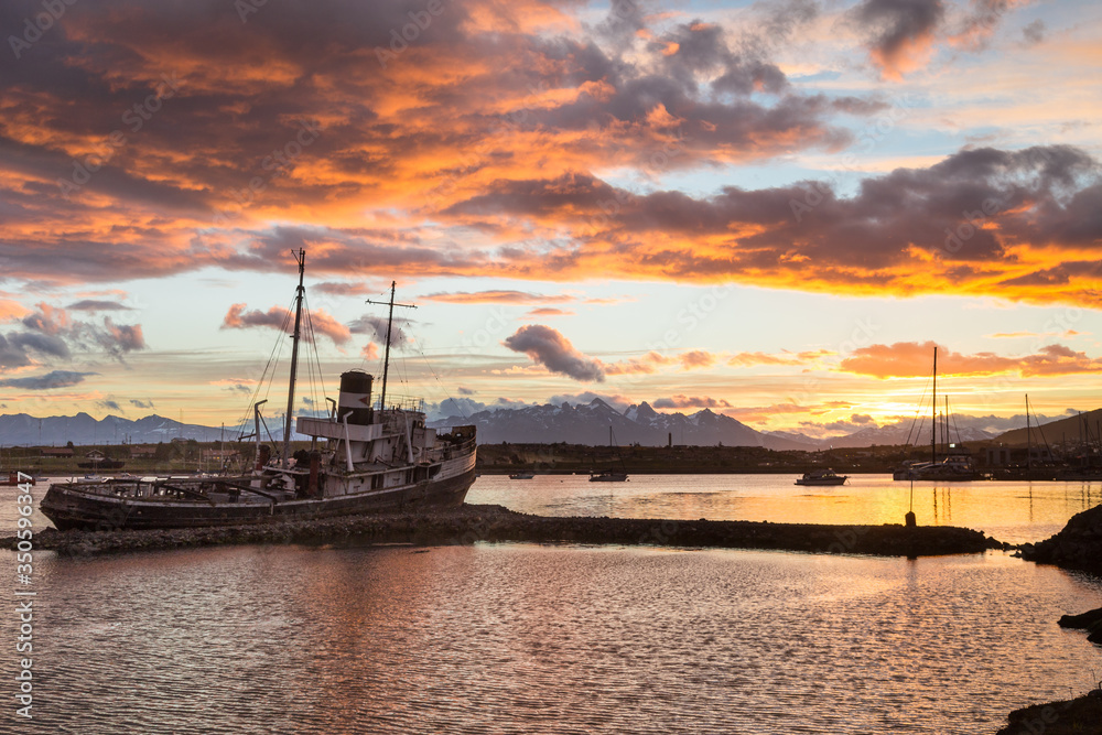 Old shipwreck in Ushuaia bay of Beagle channel on sunset with beautiful scenic mountain view on background, Tierra del Fuego province, Argentina