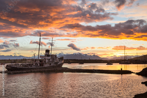 Old shipwreck in Ushuaia bay of Beagle channel on sunset with beautiful scenic mountain view on background, Tierra del Fuego province, Argentina