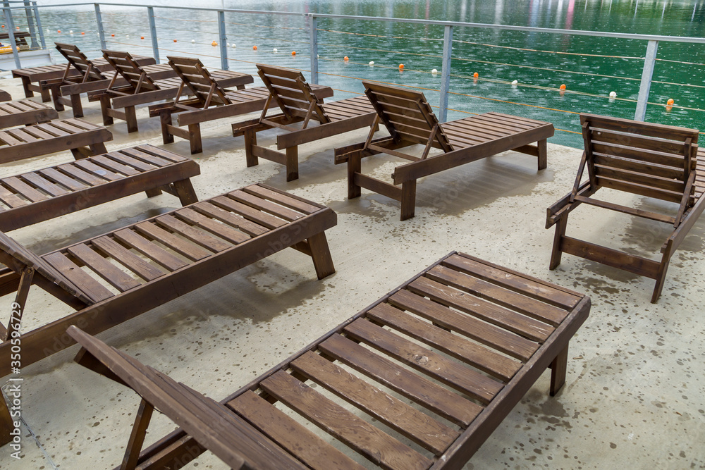 Row of empty wooden beach chairs near water.