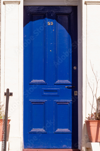 House number 53 on a royal blue wooden front door with vertical lines in London with white frame and facade photo