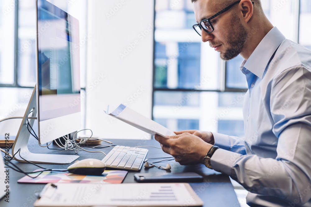 Obraz premium Formal executive reading documents against computer in office