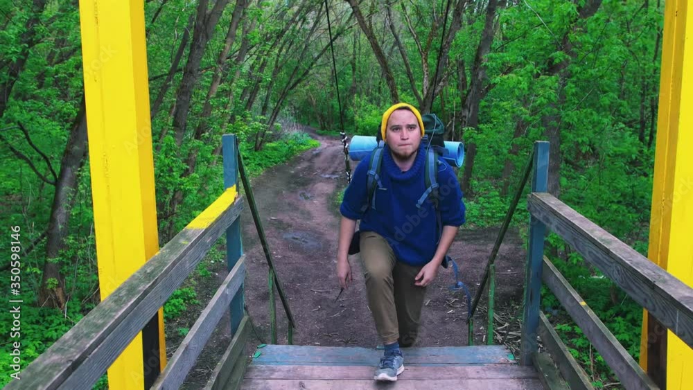 Young man traveler with a backpack walking on the bridge in the forest Young man traveler with a backpack walking on the bridge in the forest