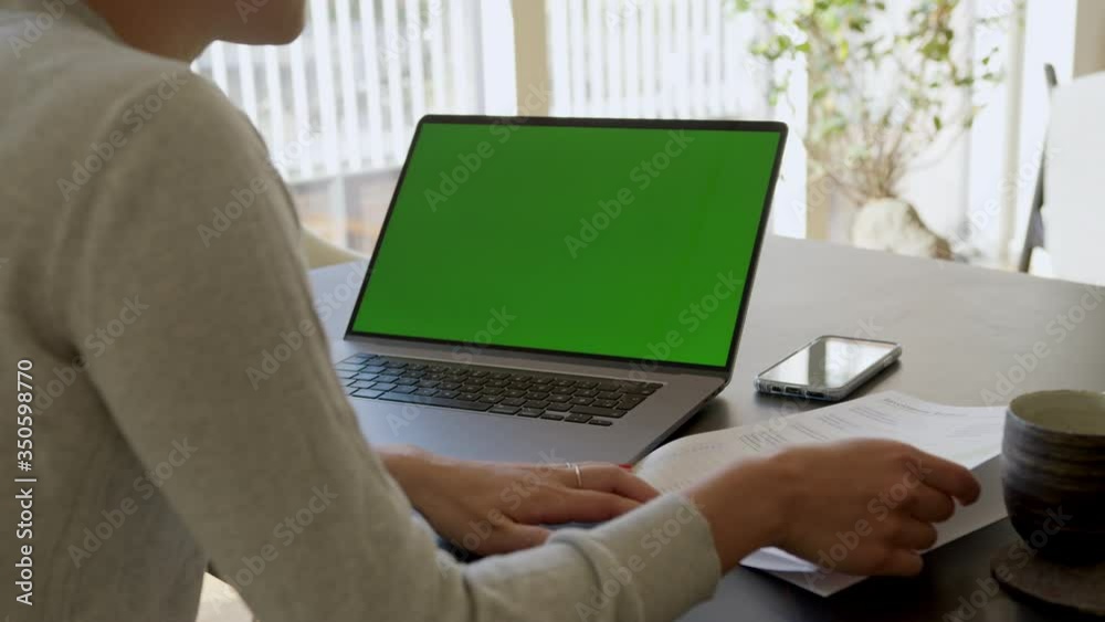 Rear view of woman sitting in front of laptop with green screen and looking at the documents at home. Female checking some papers while working on laptop from home.
Rear view of woman sitting in front of laptop with green screen and looking at the documents at home. Female checking some papers while working on laptop from home.