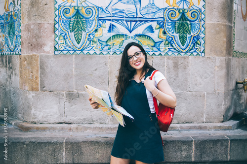 Cheerful caucasian woman in eyewear looking at camera enjoying free time on traveling hobby on vacations, half length portrait of smiling 20 female tourist using map searching historical places #350598990