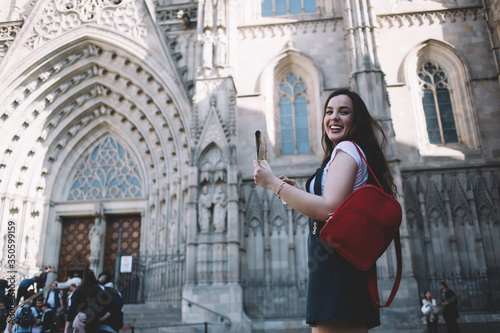 Portrait of cheerful caucasian female traveler excited with exploring old city architecture during vacation journey, smiling beautiful woman 20s tourist standing on square with backpack and map
