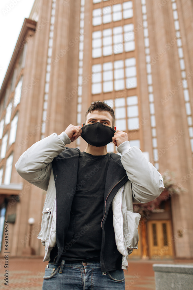 Brunette guy in a black tracksuit puts on a face mask. Black stylish face mask during a pandemic virus crown. Handmade cotton face mask for protection against viruses and bacteria. Brunette guy in a black tracksuit puts on a face mask. Black stylish face mask during a pandemic virus crown. Handmade cotton face mask for protection against viruses and bacteria.