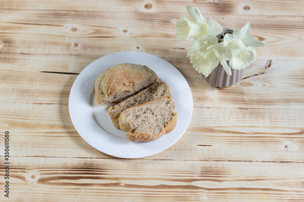 Fototapeta premium bread slices in white plate on a wooden table and daffadils in vase