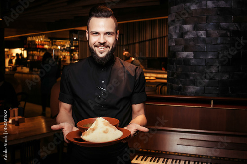 Cheerful bearded waiter with rich tomato soup with beef, rice. A discerning waiter in black clothes, with a beard and a tomato soup