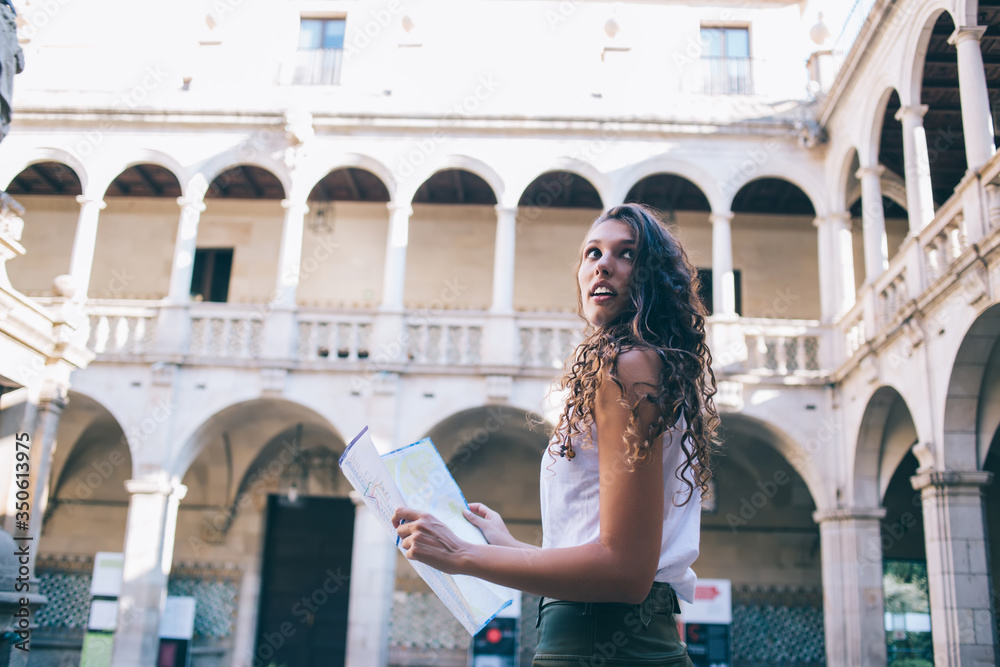 Rear view of female traveler walking with map during sightseeing tour in city visiting town on vacations, beautiful female 20s tourist strolling searching locations and directions for exploring